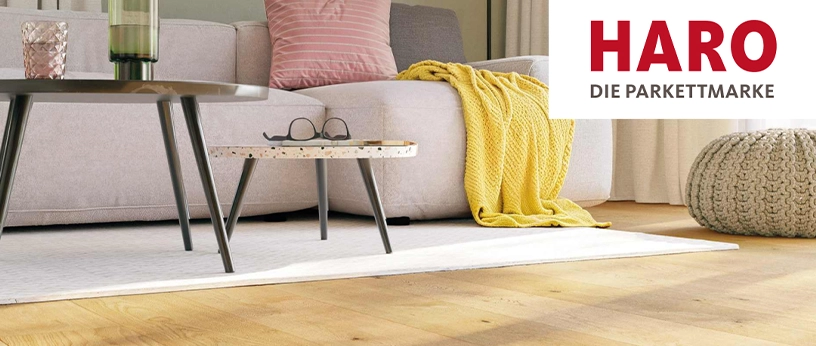 Wohnzimmerszene mit Sofa, Couchtisch und gelber Decke auf hellem Parkettboden; HARO Logo „Die Parkettmarke“ eingeblendet.